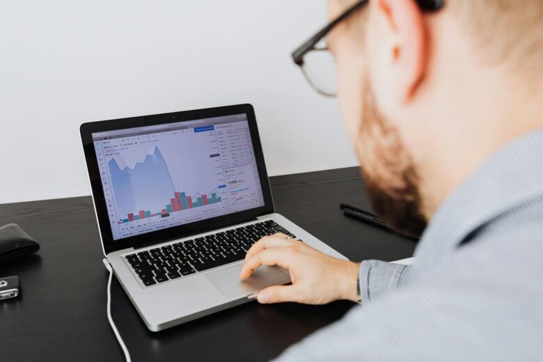 Man working on a laptop analyzing business data and financial graphs indoors.