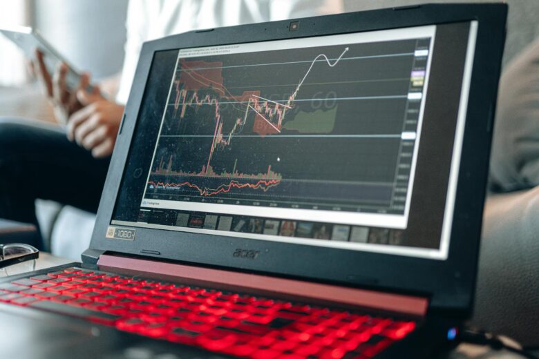 Close-up of a laptop displaying stock charts with a person in background.