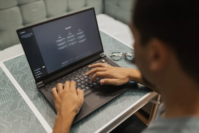 Profissional digitando em laptop enquanto consulta um assistente de inteligência artificial no ambiente de trabalho