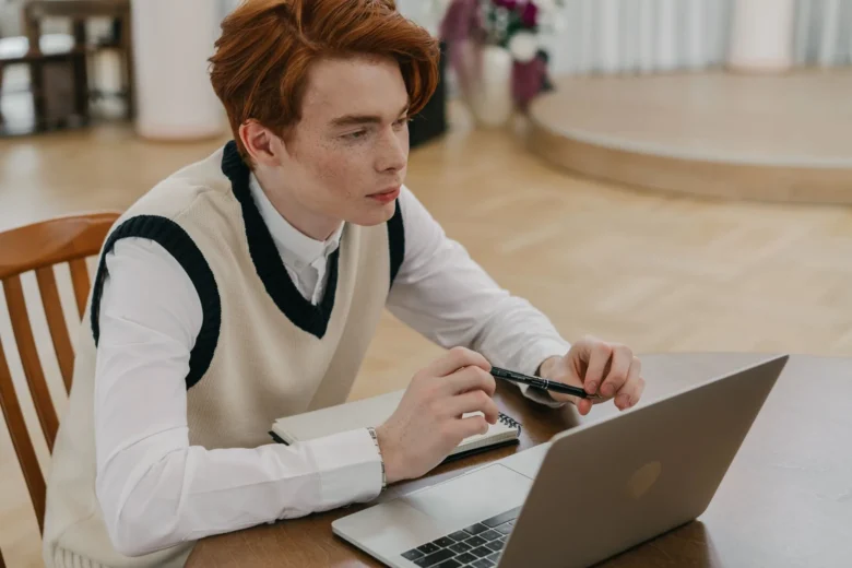 Estudante revisando anotações em caderno com laptop aberto ao lado, preparação para provas.