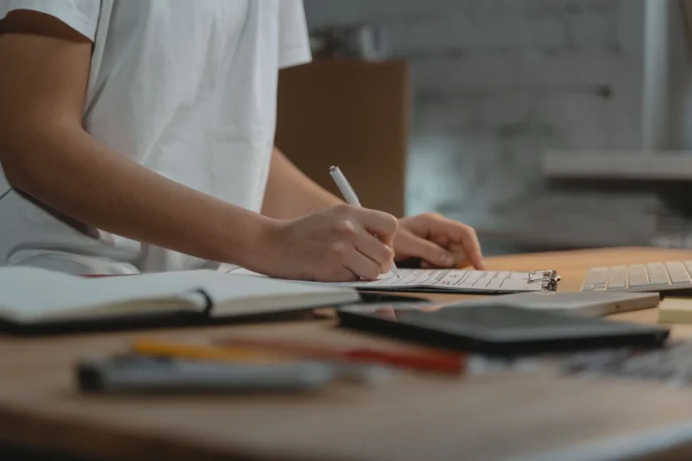 Empreendedora anota critérios de validação de uma ideia em um caderno sobre a mesa, ao lado de um celular e uma xícara de café.