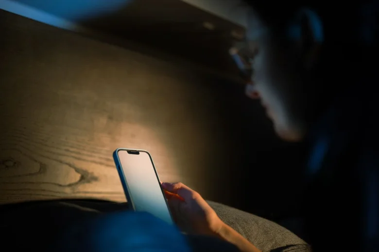 Pessoa visivelmente preocupada atende uma ligação no celular em uma mesa de casa