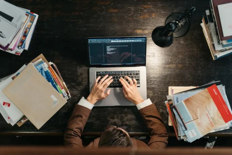 Pessoa estudando programação de modelos de linguagem em um laptop, com caderno de anotações e café ao lado
