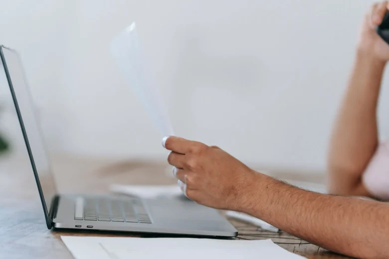 Mão digitando uma pergunta em um notebook enquanto documentos e pastas aparecem na tela, representando a busca em base própria antes da resposta da IA